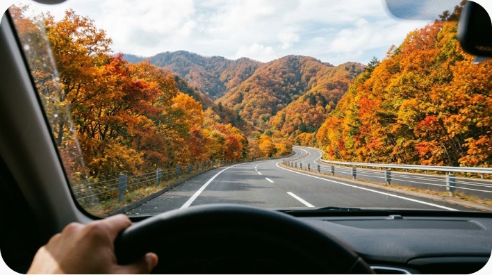 紅葉した山々を背景に走る車、フロントガラス越しの視点