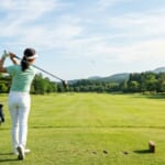 高原の広いフェアウェイに向かってドライバーを振る女性ゴルファー