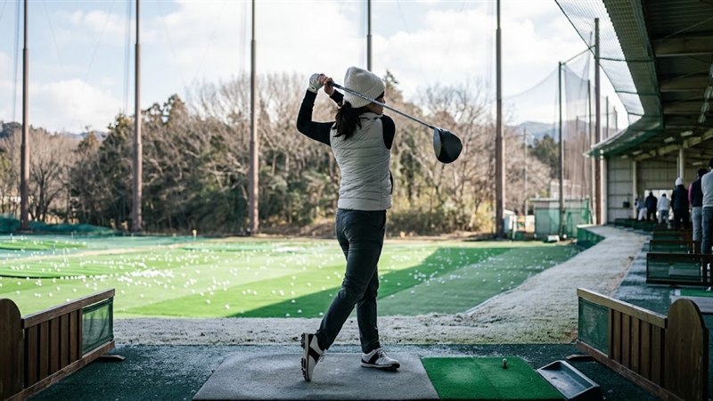 中綿ベストに薄手の長袖を合わせ、打ちっぱなしでドライバーを振る女性ゴルファー